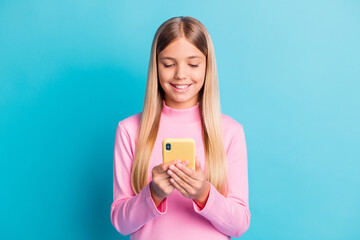 Photo portrait of smiling blonde little girl using smartphone app typing texting isolated on vivid turquoise color background