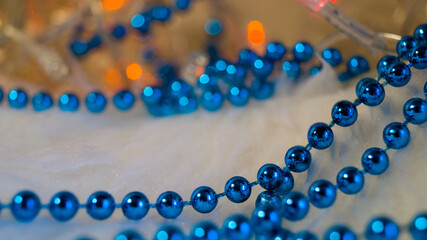 Blue Christmas beads on a light background, lit by lights of a garland. Template for a postcard. Christmas background. Place for text. Selective focus.