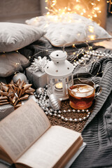 Beautiful Christmas still life. A cup of hot tea with a knitted sixth blanket on a warm floor among New Year's gifts and lights. Cozy flatlay. Christmas home cooking concept