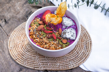 Healthy breakfast Purple smoothie bowl: Dragon fruit smoothie with banana, coconut, almonds, sunflower and chia seeds and strawberry