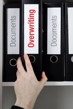 Overwriting. File Folder is taking by a hand from office shelf. Red Text is on the label of the documents.