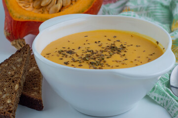 Pumpkin soup in a white plate with slices of dark seed bread in the background pumpkin.