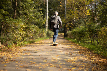 Fototapeta premium Mature man in headphones skateboarding in wood