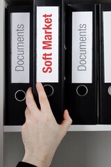 Soft Market. File Folder is taking by a hand from office shelf. Red Text is on the label of the...