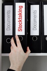 Stocktaking. File Folder is taking by a hand from office shelf. Red Text is on the label of the...
