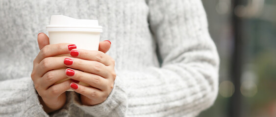 female hand holding paper cup of take away drinking coffee on city background. space place for your text or logo.