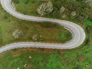 Winding narrow road on a hill in Burren, Ireland. Aerial drone view. Green fields and small trees around the pass.