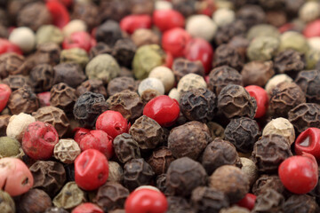 Side view of pile of various peppercorns, close up. Mix of black, white, green and red dried peppercorns.