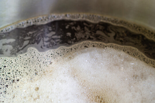 Close-up of craft beer and foam in a fermentation container. Process of making home beer from malt. Craft beer from barley and dark malt. Selective focus