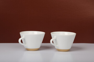 Two white ceramic coffee cups on whit table against brown background