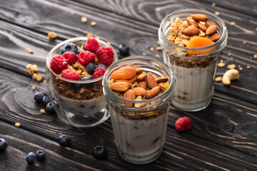 Delicious granola with berries, dried apricots, nuts and yogurt in glass cups on wooden surface