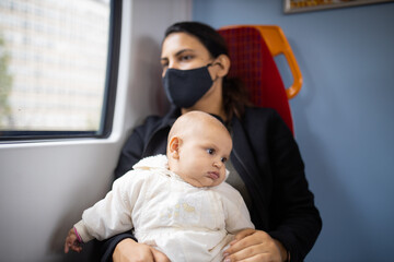 Woman sitting next to a window in a bus and holding her baby in her arms