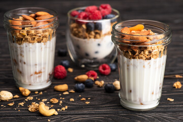 delicious granola with dried apricots, nuts and yogurt in glass cups on wooden surface on blurred...