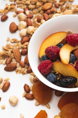 delicious granola with nuts, berries and fruits in bowl on white