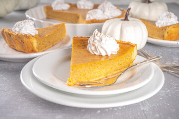Traditional Autumn Pumpkin Pie. Homemade American Pumpkin pie topped with Whipped Cream. Rustic wooden table bakcground with Cozy plaid and sweater.