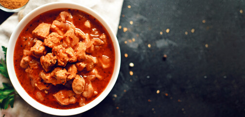 Indian food. Chicken Tikka Masala in a white bowl on a dark background. Appetizing meat with curry and tomato sauce, gravy with various spices. copyspace. close-up, top view