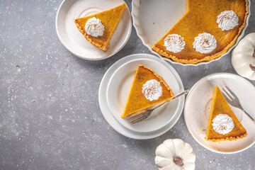 Traditional Autumn Pumpkin Pie. Homemade American Pumpkin pie topped with Whipped Cream. Rustic wooden table bakcground with Cozy plaid and sweater.