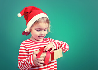 little child in santa hat holding gift box,kid opening new year present.Empty space  x mas backdrop.