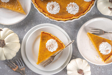 Traditional Autumn Pumpkin Pie. Homemade American Pumpkin pie topped with Whipped Cream. Rustic wooden table bakcground with Cozy plaid and sweater.