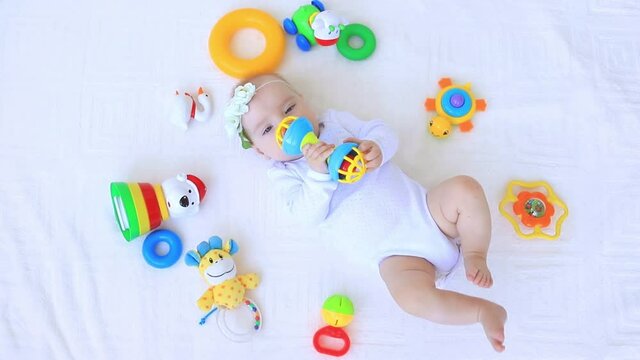 a child plays with a rattle on a white bed among toys