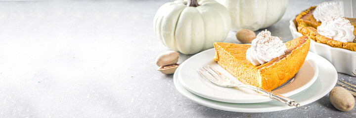 Traditional Autumn Pumpkin Pie. Homemade American Pumpkin pie topped with Whipped Cream. Rustic wooden table bakcground with Cozy plaid and sweater. - obrazy, fototapety, plakaty