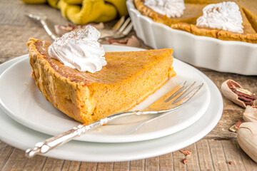 Traditional Autumn Pumpkin Pie. Homemade American Pumpkin pie topped with Whipped Cream. Rustic wooden table bakcground with Cozy plaid and sweater.