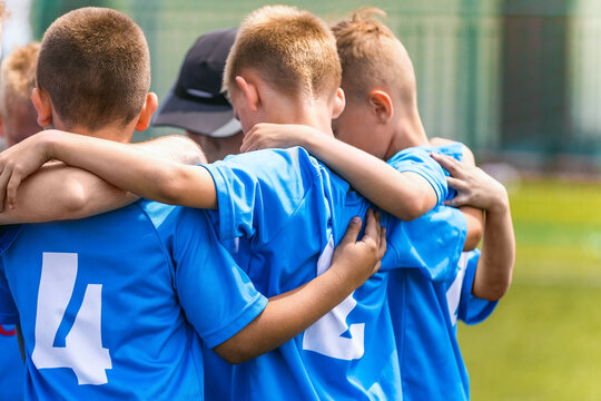 Kids soccer team with coach in group huddle before the match. Elementary age children are listening together to coach motivational speech. Boys in blue football shirts © matimix