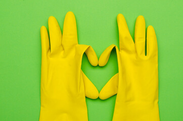 Top view of yelllow protective gloves for cleaning and shape of heart on the green surface