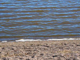 Low waves with foam hit the pebble shore, closeup