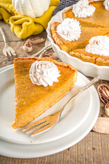 Traditional Autumn Pumpkin Pie. Homemade American Pumpkin pie topped with Whipped Cream. Rustic wooden table bakcground with Cozy plaid and sweater.