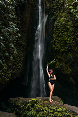 Beautiful girl at a waterfall on the island of Bali Indonesia. Sexy woman at the waterfall. Young and beautiful girl in bikini taking bath in a waterfall. Beautiful woman posing at a waterfall.