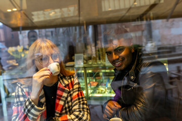 Obraz na płótnie Canvas young multiethnic couple is having breakfast sitting in a cafe