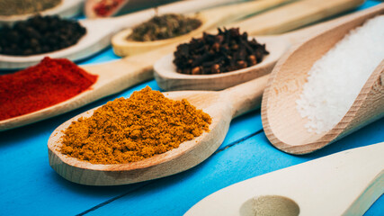 curry powder in the kitchen spoon between various spices on the blue background. Close up.