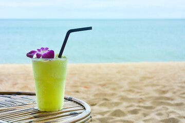 green color smoothie with purple orchid on the wooden table with the beautiful sea background, copy space
