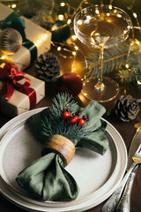 Christmas table setting among gift boxes and garland lights on wooden table. Concept of Christmas and New Year dinner.