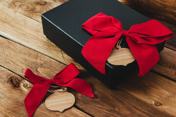 Regalo en caja negra con lazo rojo y fondo en madera 