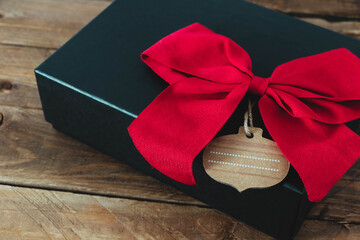 Regalo en caja negra con lazo rojo y fondo en madera 