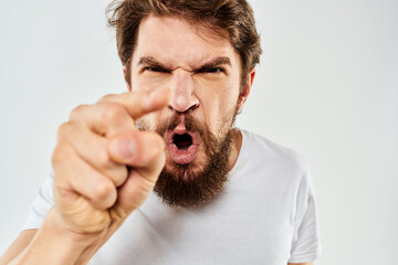 Emotional bearded man in a white t-shirt gestures with his hands light background