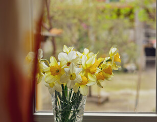 A vase of flowers on the windowsill. Yellow flowers daffodils on the window in an autumn cloudy day