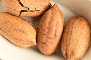 Several organic ripe pecans on a faience plate close-up, on a white wooden table.