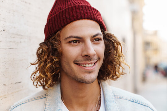 Smiling young curly man walking outdoors by street.
