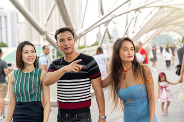Three happy young asian friends outdoor standing and walking along city bridge