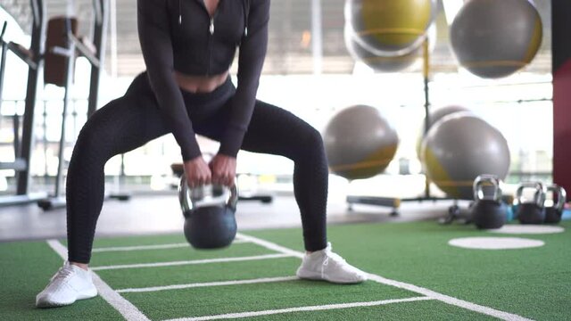 Below part of woman in sportswear exercise with kettlebell at gym
