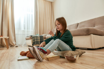 A little girl taking a gamepad to play a videogame sitting on a floor in a big bright room © Svitlana