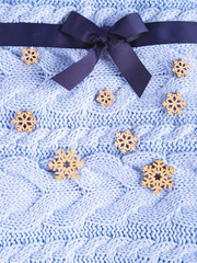 Beautiful wool knitted background in pale blue color made like a present with the ribbon and the wooden snowflakes.