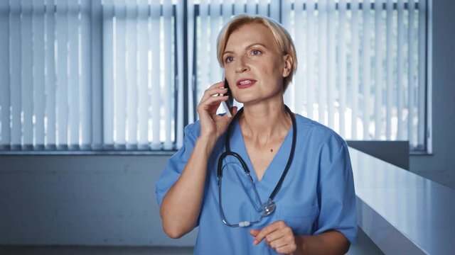 blonde and middle aged doctor talking on smartphone in clinic