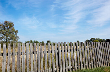 Old wooden fence against a blue sky with clouds on a sunny day. Background of old wood planks rustic
