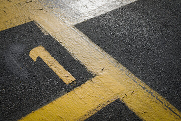 sign on the asphalt, yellow painted number one on grey street, yellow lines like a corner on the...