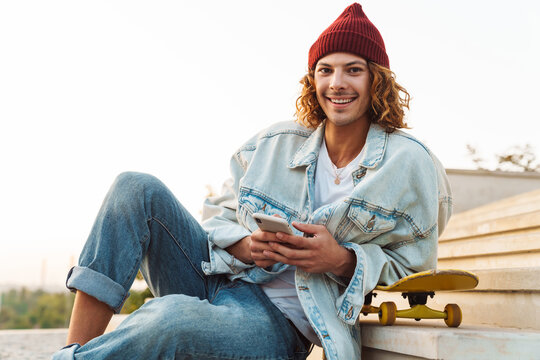Positive young curly man scater using mobile phone