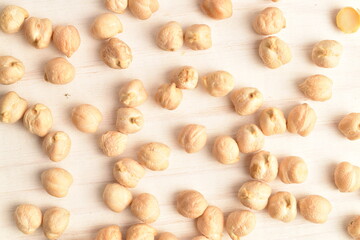 Uncooked hummus grains, close-up, on a white wooden table.